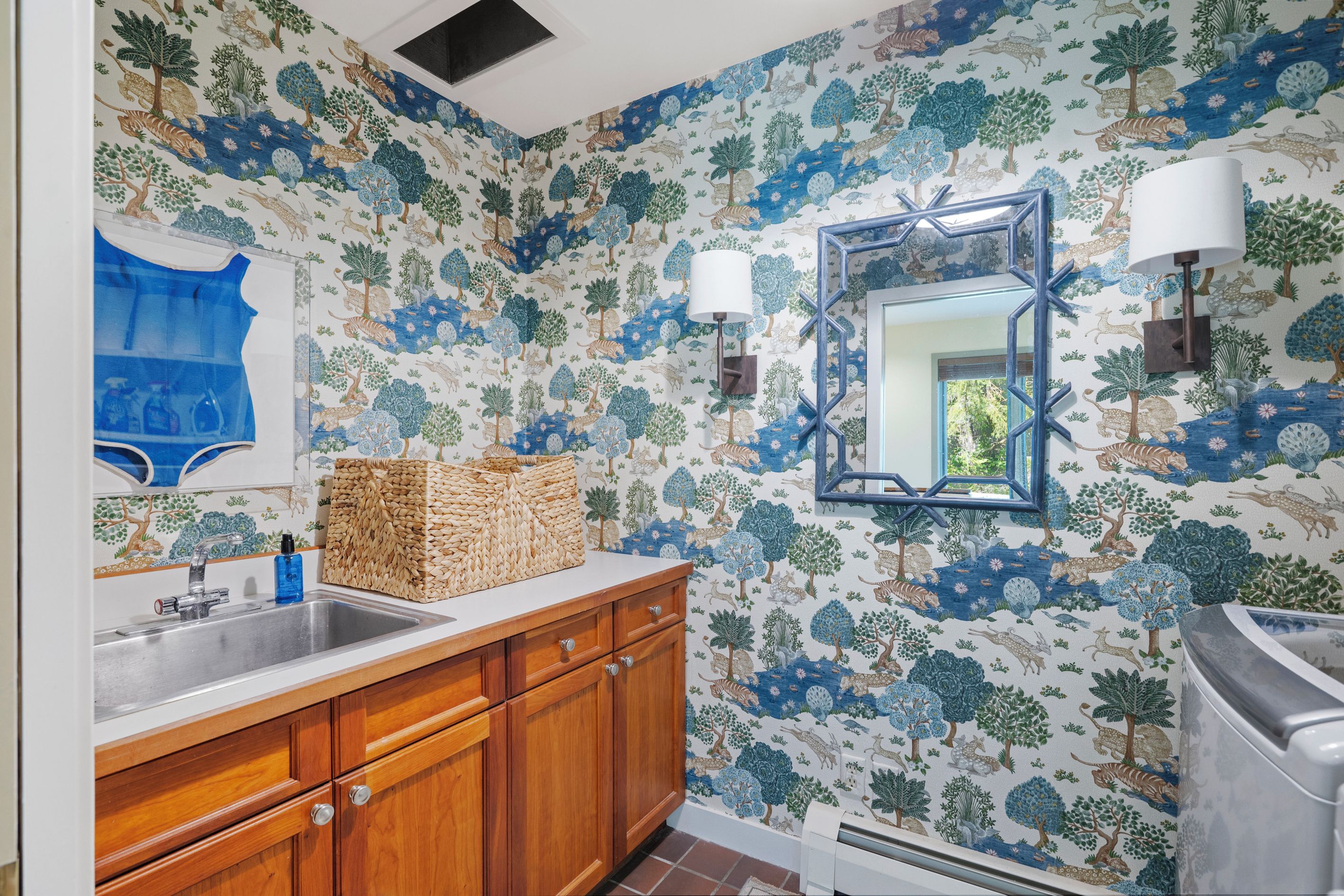 Une salle de bain avec un papier peint à motifs, des meubles en bois, un lavabo et un miroir agrémenté de luminaires fixés au mur.