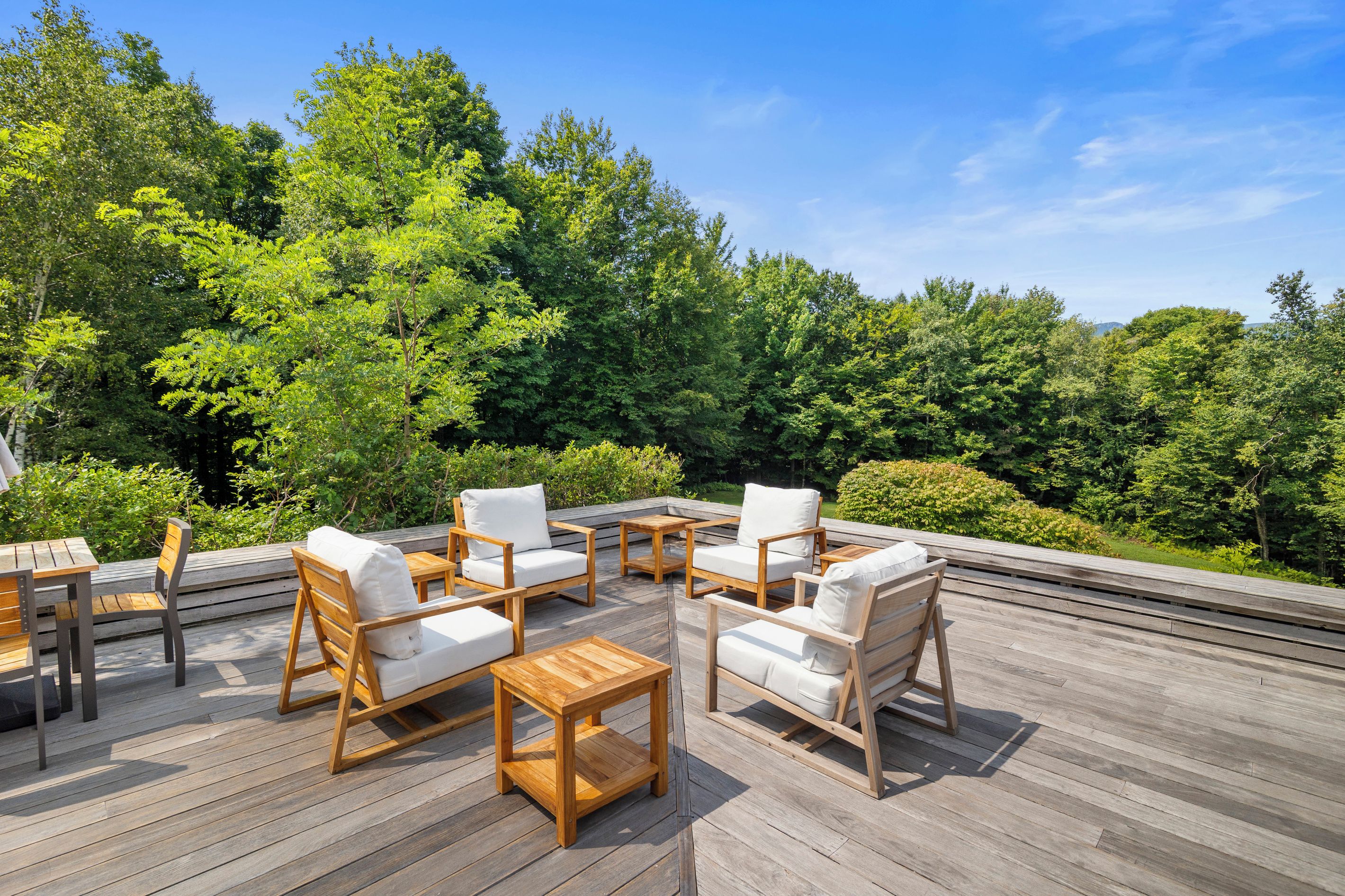 Terraza exterior con mobiliario de madera y vista a un bosque.