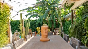 An outdoor dining area with a wooden table and wicker chairs, surrounded by lush greenery and cacti. - Private 420 Pool & Spa Bungalow: Botanical Oasis (Los Angeles)
