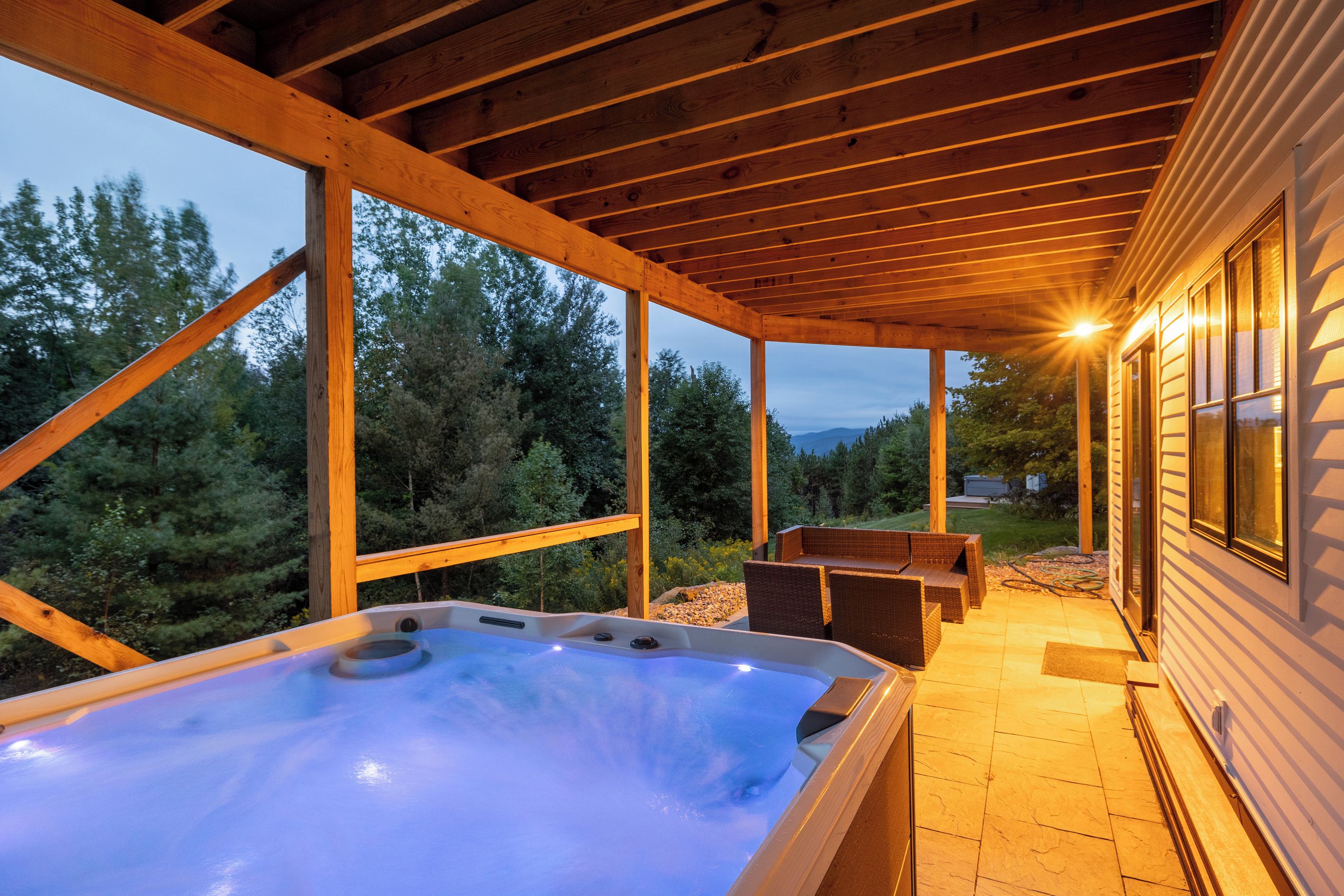 A hot tub under a wooden pergola with a view of trees and a mountain in the background.