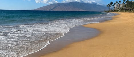 A beach with a mountain in the background, clear skies, and a calm sea.