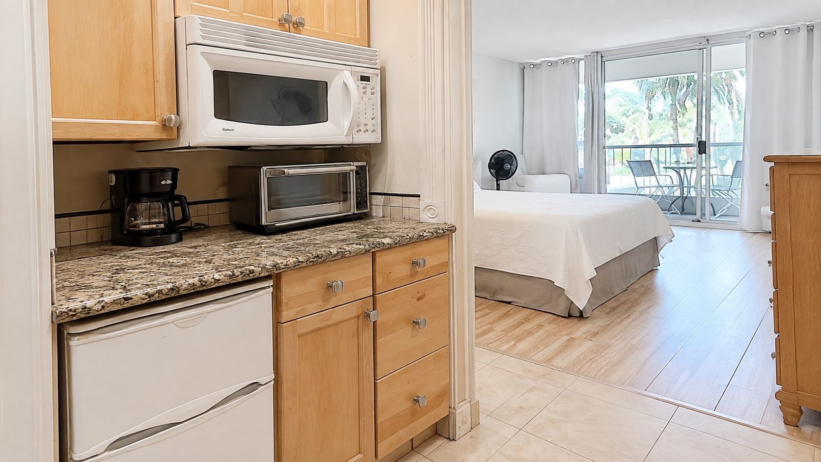 Una cocina equipada con microondas y cafetera, y una cama con vista al balcón.