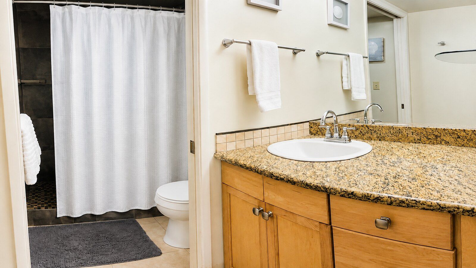 Un baño con cortina de ducha, inodoro, lavamanos con encimera de granito y armarios de madera.