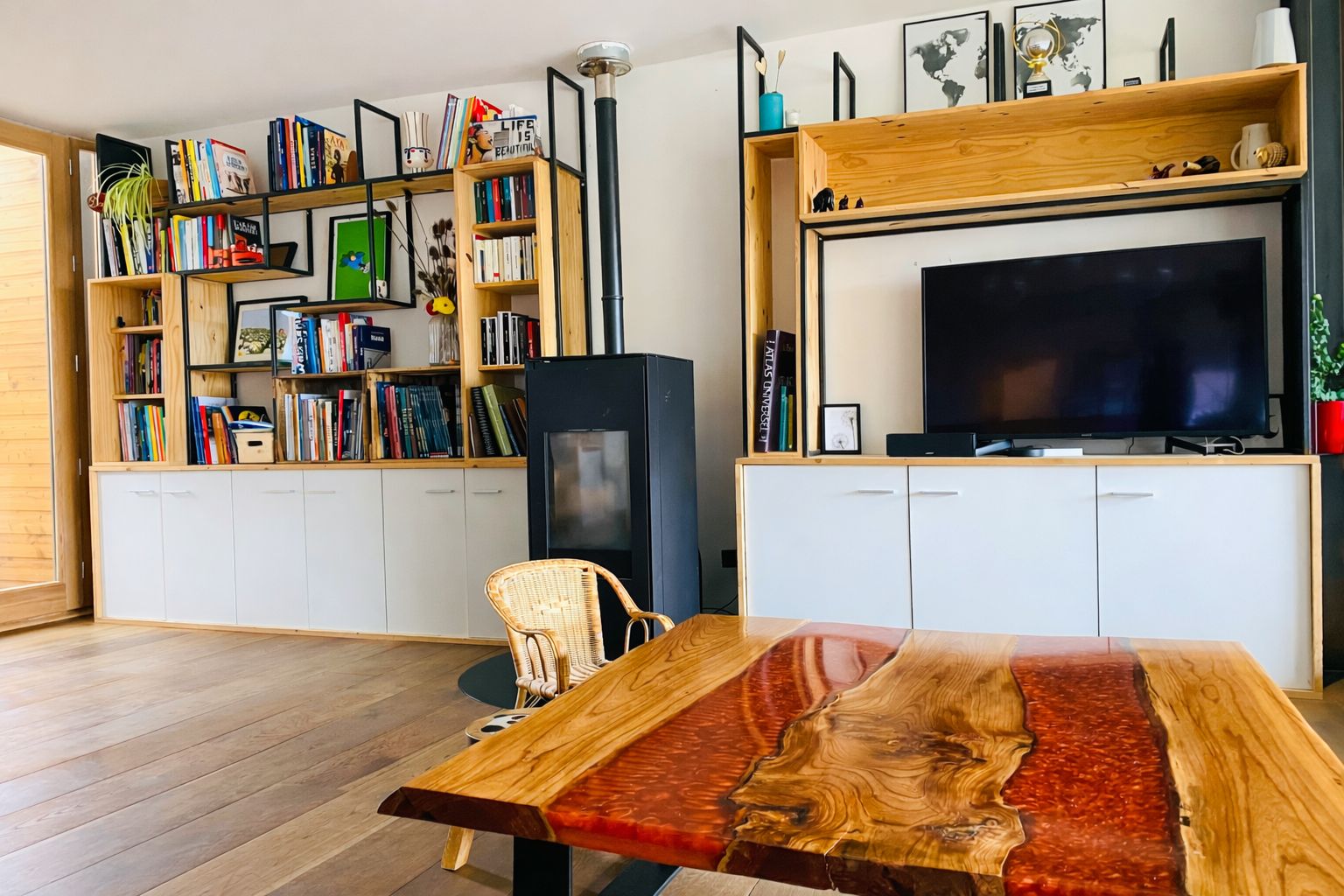 Un salon moderne avec une table basse en bois, une bibliothèque, un téléviseur à écran plat et un fauteuil en osier.