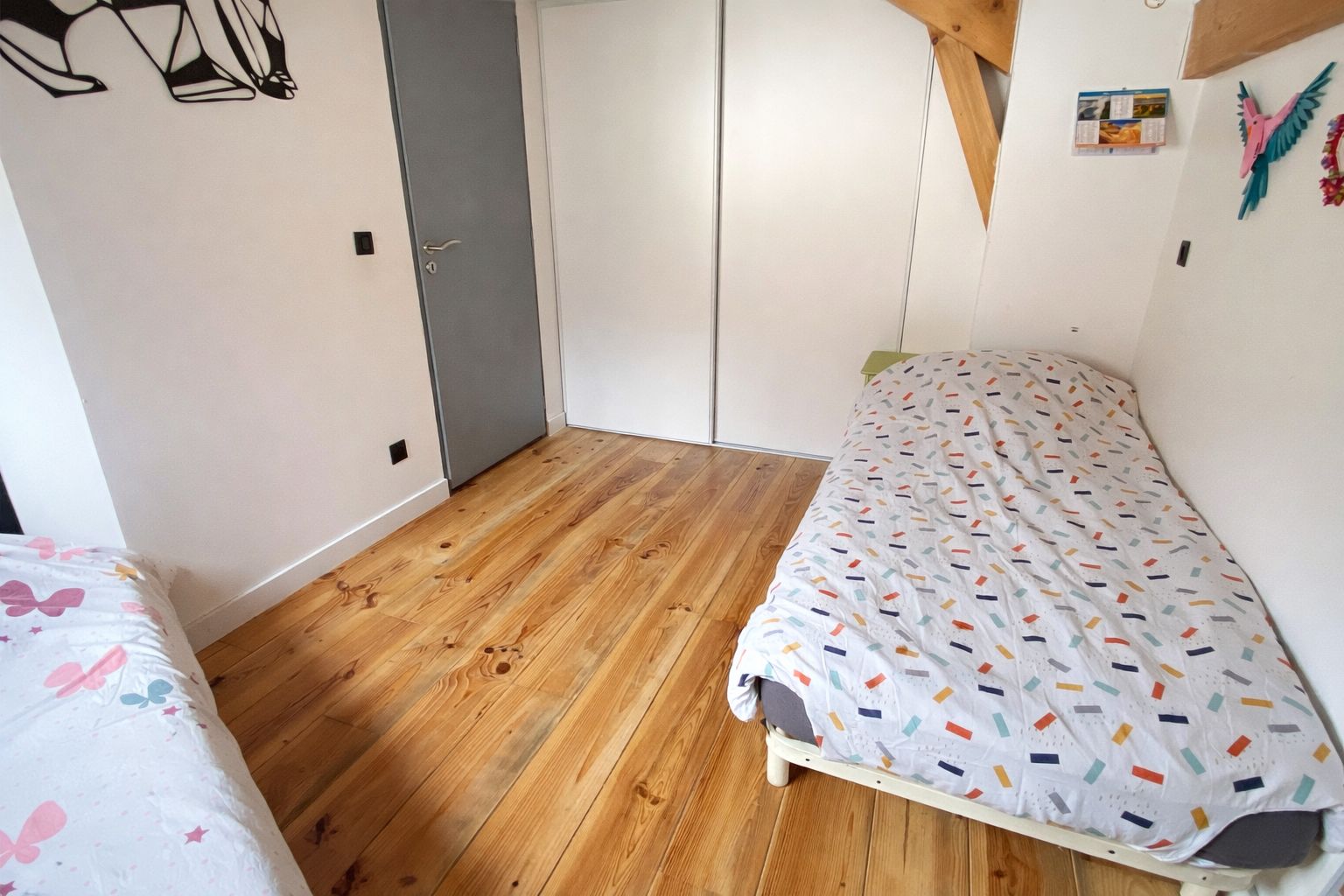 A bedroom with two beds, wooden flooring, and a grey door.
