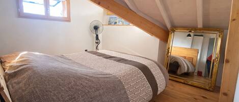 A bedroom with a bed, a fan, a window, and a mirror.