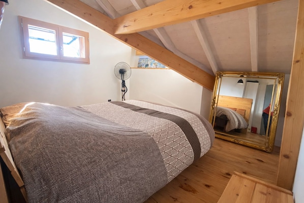 A bedroom with a bed, a fan, a window, and a mirror.