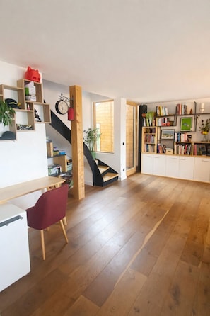 A spacious room with a wooden floor, a red chair, a desk, a bookshelf, and a staircase.