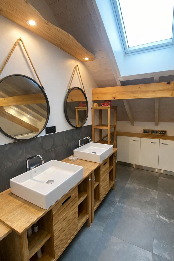 A modern bathroom with two sinks, wooden cabinets, and a skylight.