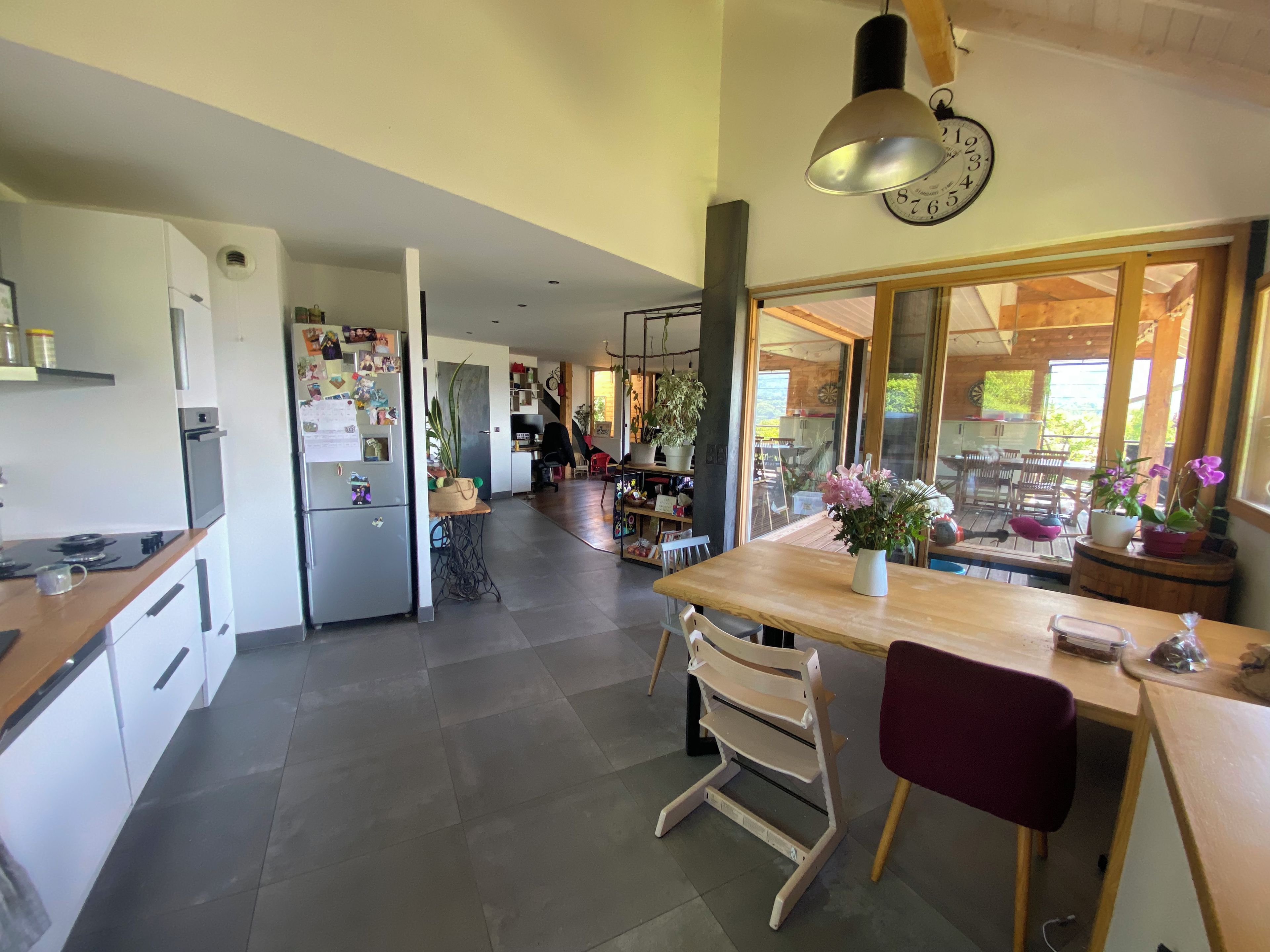A modern kitchen with a dining area, a clock on the wall, and a view of the outdoors.