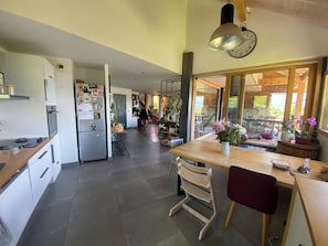 A modern kitchen with a dining area, a clock on the wall, and a view of the outdoors.