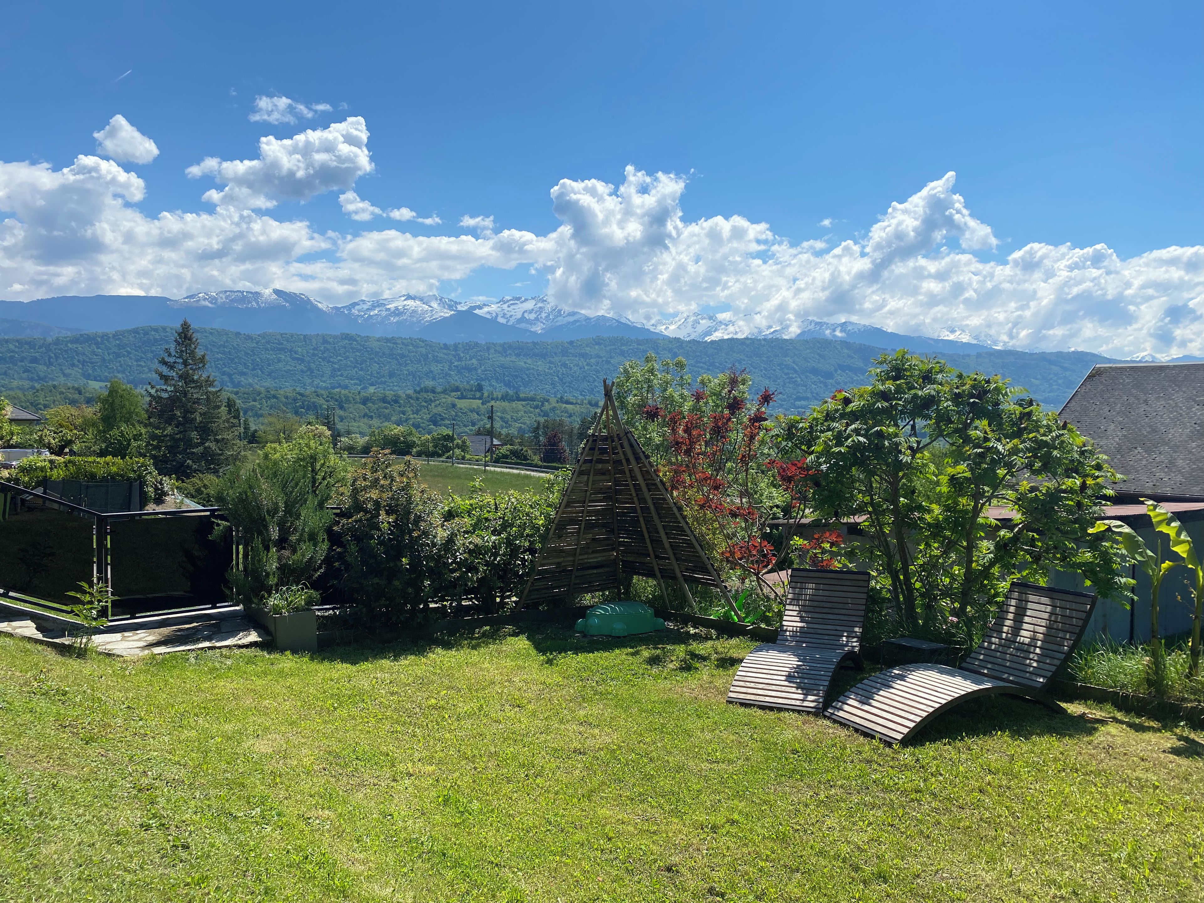 Una zona erbosa all'aperto con una struttura in legno, vista sulle montagne e cielo sereno.