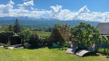 Una zona erbosa all'aperto con una struttura in legno, vista sulle montagne e cielo sereno.