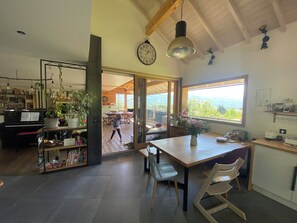 A spacious kitchen with a dining area, wooden beams, a large window, and a view of the outdoors.
