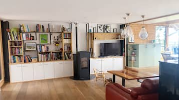 A modern living room with a fireplace, bookshelves, a television, and a dining area.