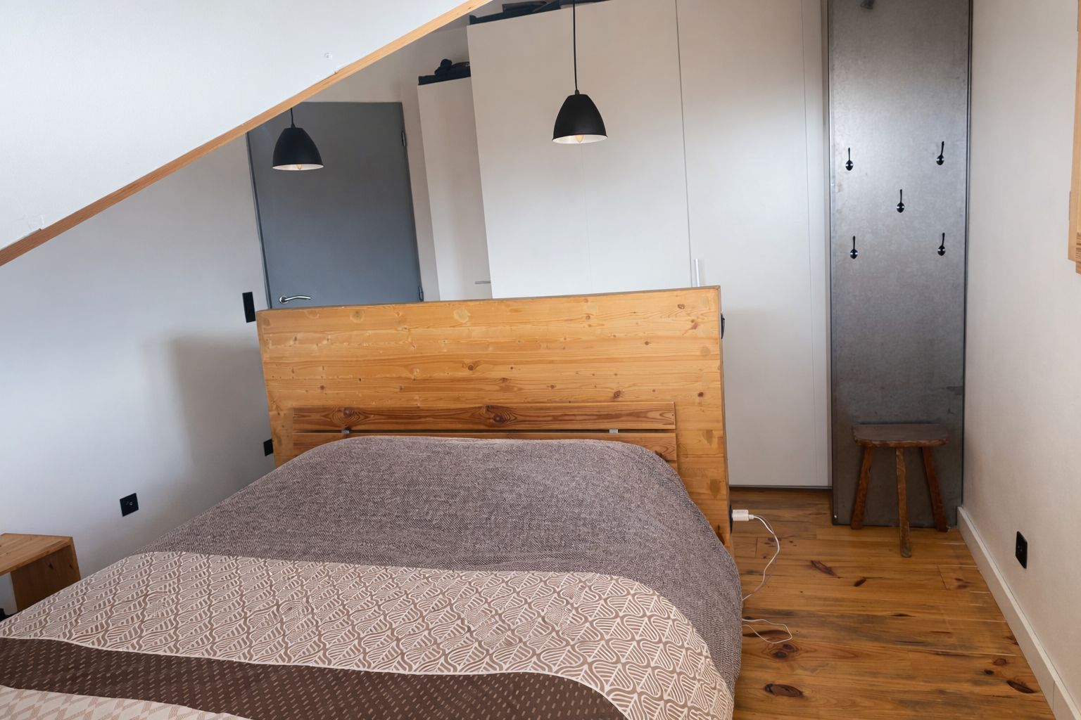 A bedroom with a wooden headboard, a patterned bedspread, and a small stool.