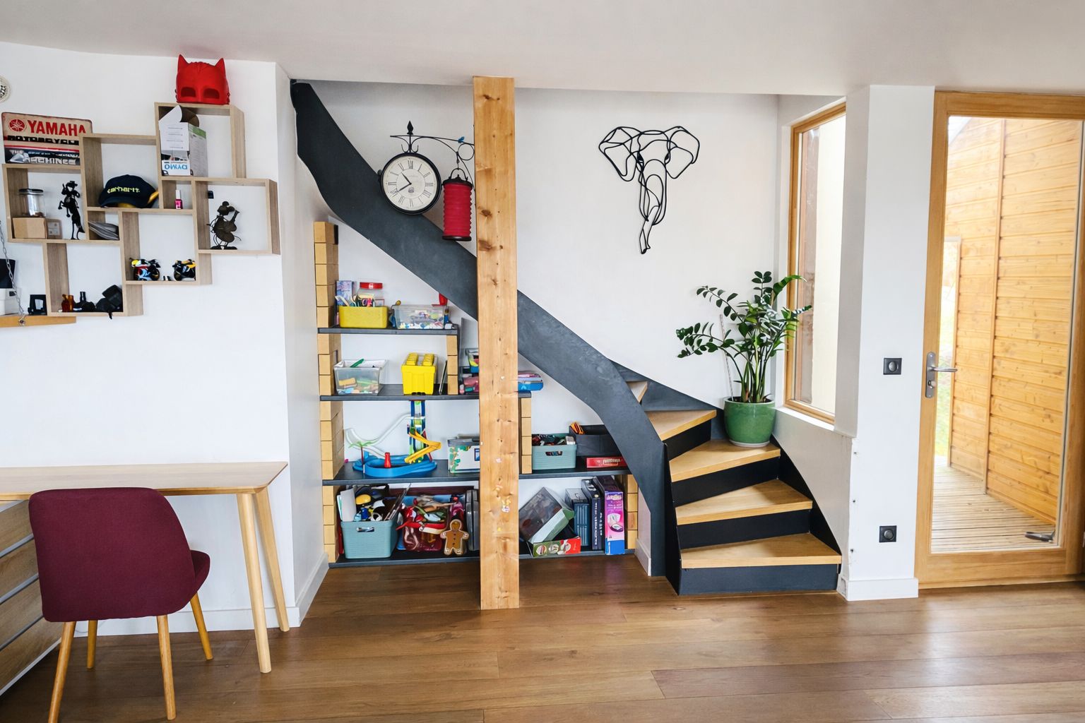 Un interno moderno con una scala in legno, una scrivania con una sedia e una libreria piena di oggetti diversi.