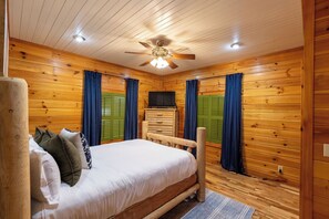 A wooden-paneled room with a bed, a television, and a ceiling fan. - Asheville luxury cabin with Mountain View  hot tub game room patio and sauna (Candler)