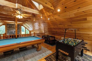 A wooden interior with a pool table, foosball table, and a stone wall. - Asheville luxury cabin with Mountain View  hot tub game room patio and sauna (Candler)