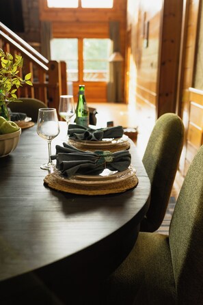 A wooden dining table with a glass of wine, a bottle, and a bowl of fruit. - Asheville luxury cabin with Mountain View  hot tub game room patio and sauna (Candler)