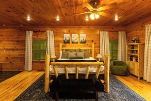 Ein Schlafzimmer einer Holzhütte mit einem Bett, einer Bank, einem Deckenventilator und einem Bücherregal.