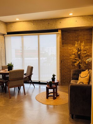A living room with a dining area, a brick wall, a large window, and a plant. - Apartment 206, Akron Stadium, UP, Aquatic Center, Exit to Vallarta, Pet-Friendly, (Zapopan)
