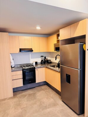 A modern kitchen with wooden cabinets, a stainless steel refrigerator, a built-in oven, and a granite countertop. - Apartment 206, Akron Stadium, UP, Aquatic Center, Exit to Vallarta, Pet-Friendly, (Zapopan)