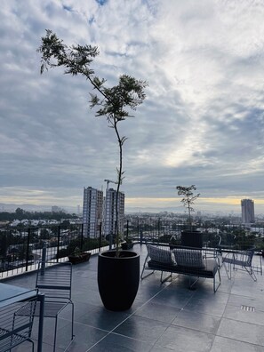 A rooftop terrace with a potted tree, seating area, and a cityscape view. - Apartment 206, Akron Stadium, UP, Aquatic Center, Exit to Vallarta, Pet-Friendly, (Zapopan)