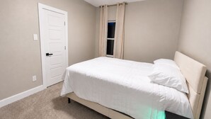Un dormitori amb un llit, una porta i una finestra amb cortines.
