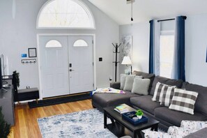 Un salon moderne avec un canapé gris, une table basse, un tapis et une grande fenêtre avec des rideaux.