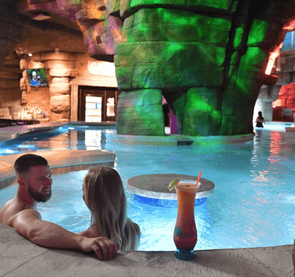 A man and a woman relaxing by a pool with a drink on the edge.