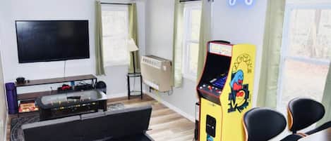 Een kamer met een flatscreen televisie, een tafelvoetbaltafel, een spelconsole en een klein tafeltje met stoelen.