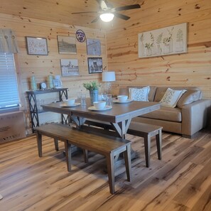 Ein gemütliches Zimmer mit Holzbalkendecke, einem Esstisch mit Bänken, einer Couch und einer Kaffeestation.