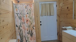 En träinredd toalett med en duschgardin med blommönster och en dörr med en gardin.