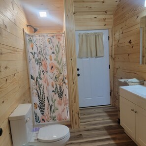 Ein Holzambiente mit Toilette, einer Duschkabine mit Blumenmuster und einer Tür mit Vorhang.