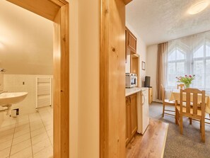Ein Zimmer mit Holztür, Spüle, Mikrowelle, Tisch mit Stühlen und einem fenster mit Vorhängen.