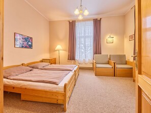 Ein Hotelzimmer mit zwei Holzbetten, einer Couch, einem Sessel, einer Lampe, einem Fenster mit Vorhängen und einem Bild an der Wand.