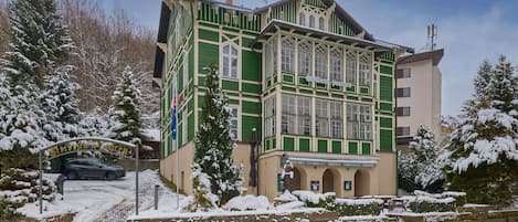 A multi-story building with a green facade, a stone wall in front, and a snow-covered landscape.