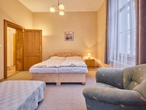 Ein Schlafzimmer mit einem Bett, zwei Nachttischen, einem Sessel, einem Fenster mit Vorhängen und einer Tür.