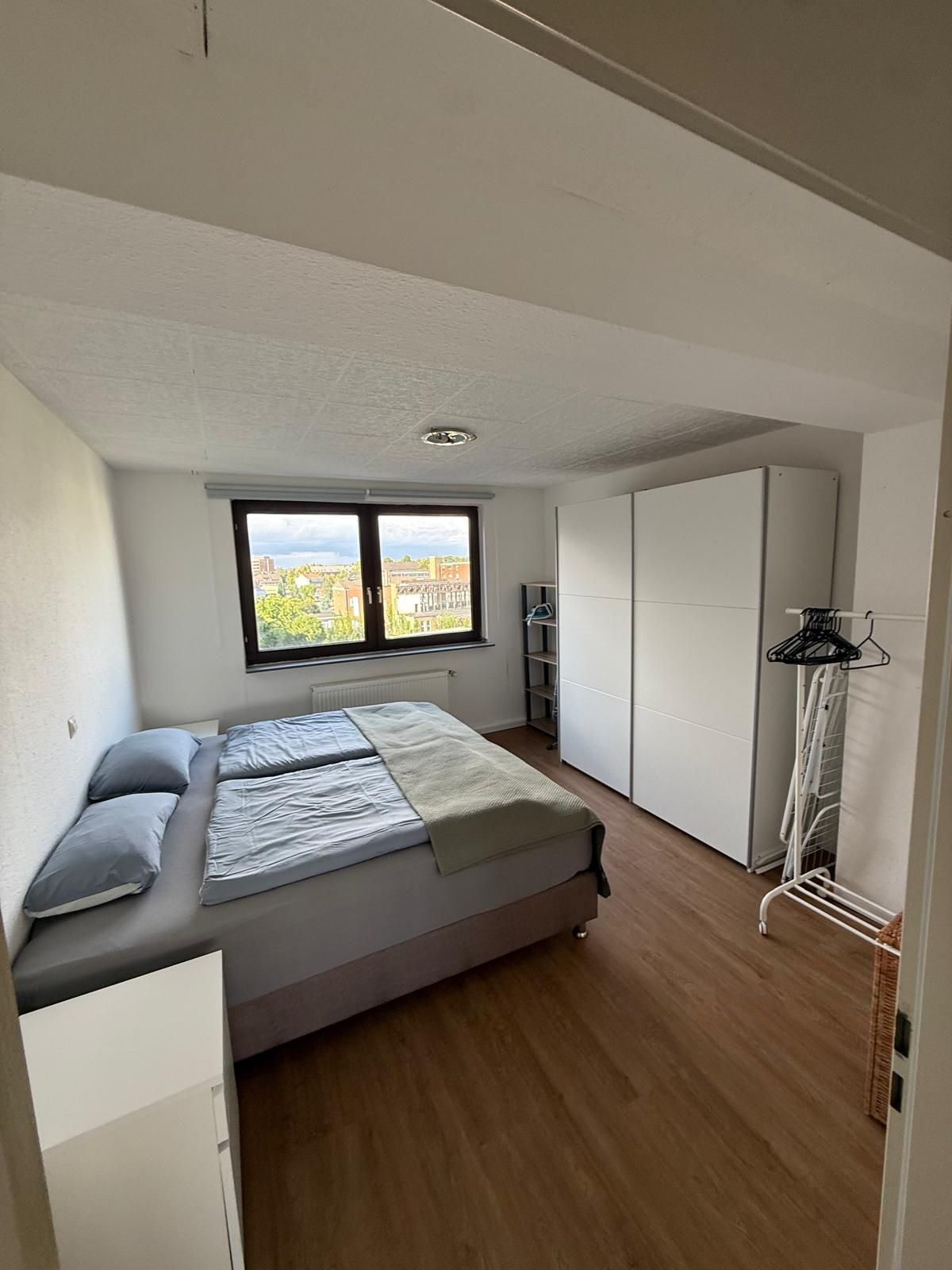 A bedroom with a bed, a window, a wardrobe, and a radiator.