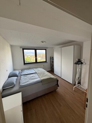 A bedroom with a bed, a window, a wardrobe, and a radiator.