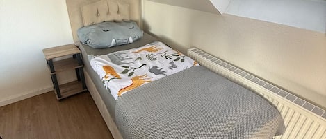 Una cama individual con cabecera, una mesita de noche y una ventana con persianas.