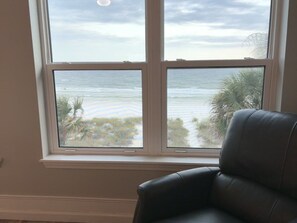 A room with a large window overlooking a beach, a black leather chair, and a white wall. - Beachfront Townhouse(22) Pet Friendly Covered Deck (Panama City)