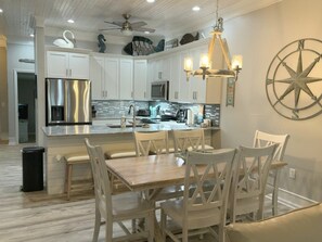 A modern kitchen with white cabinetry, a stainless steel refrigerator, and a dining area with white chairs. - Beachfront Townhouse(22) Pet Friendly Covered Deck (Panama City)