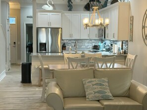 A modern kitchen with white cabinets, a stainless steel refrigerator, and a dining area with a beige sofa and chairs. - Beachfront Townhouse(22) Pet Friendly Covered Deck (Panama City)