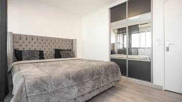Een slaapkamer met een groot bed, een kledingkast met spiegel en een schuifdeurkast.