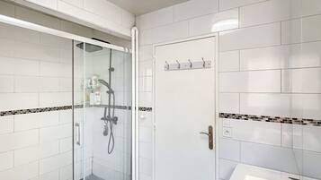 Een moderne badkamer met een douchecabine van glas, witte tegels, een wastafel en een deur met haken.