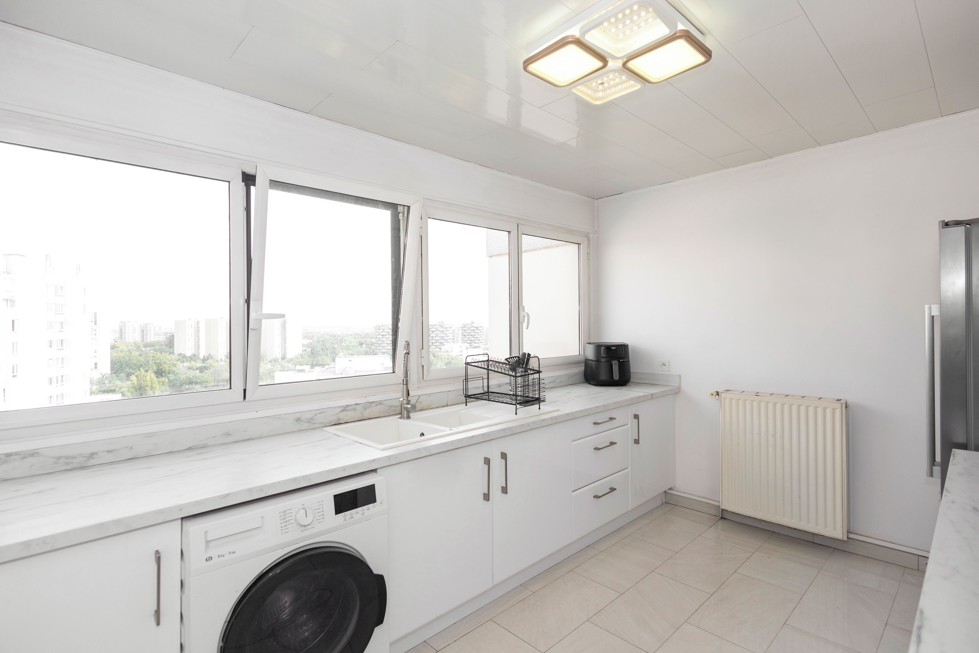 Een moderne keuken met een ingebouwde wasmachine, een spoelbak en een raam met uitzicht op een stadsgezicht.