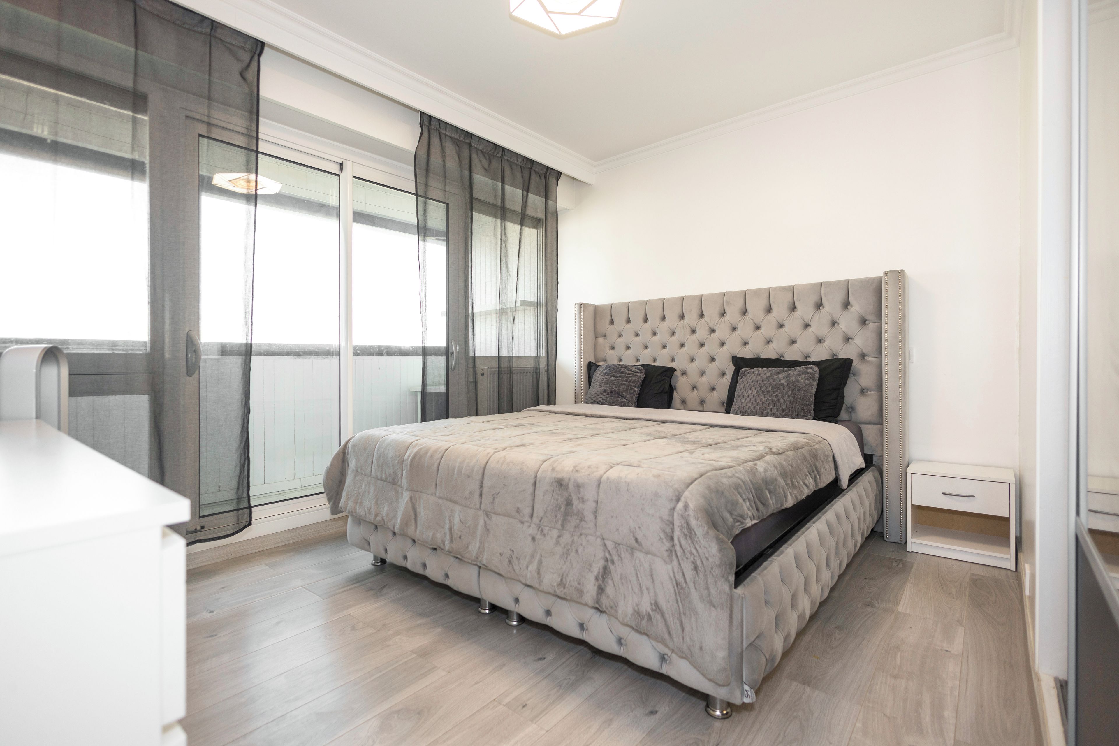 A bedroom with a large bed, a bedside table, and a window with curtains.