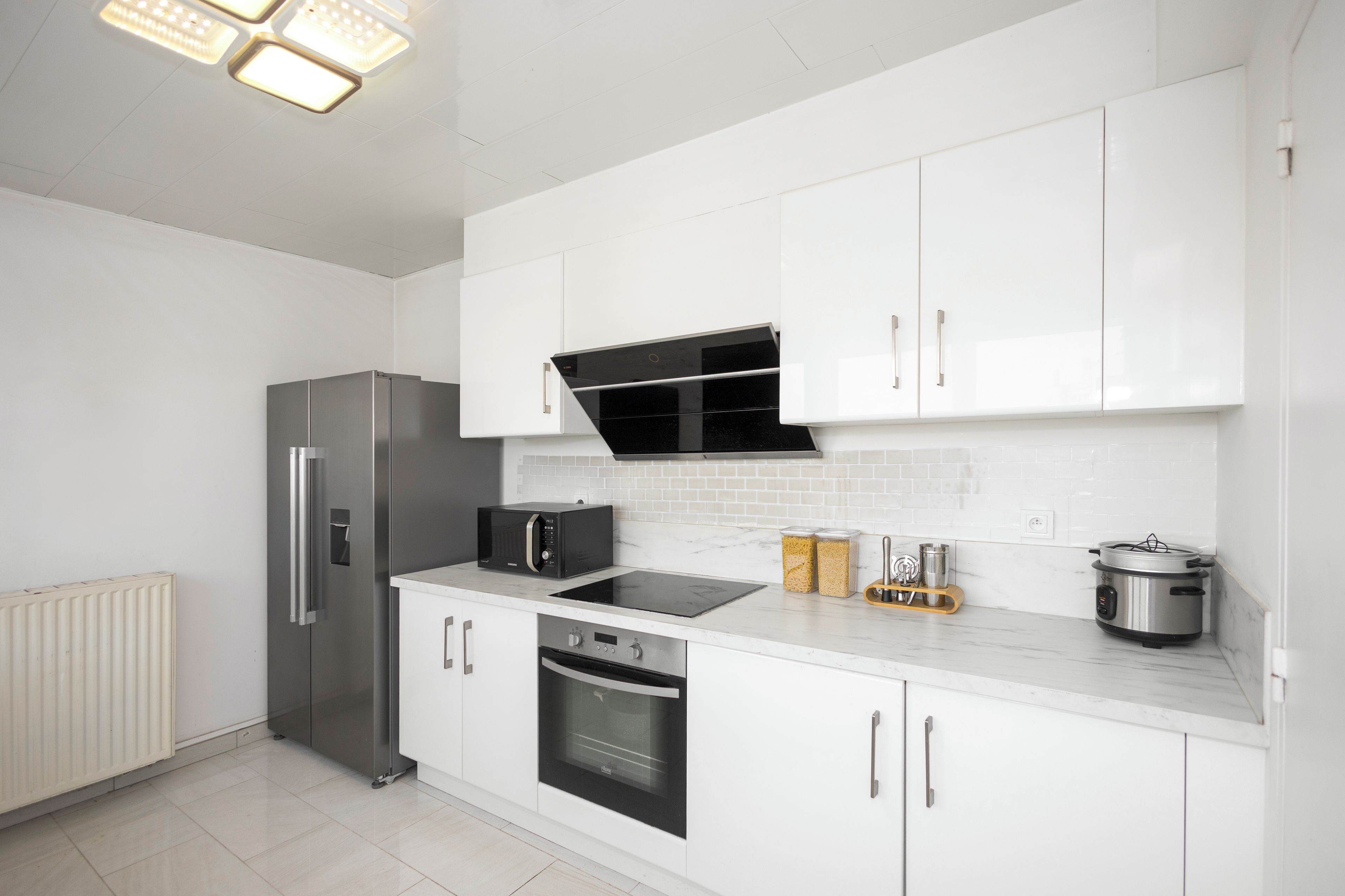 Een moderne keuken met witte kasten, een inbouwoven, een magnetron en een roestvrijstalen koelkast.